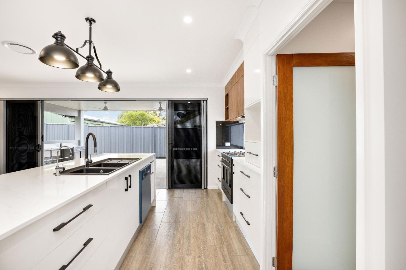 A Kitchen With White Cabinets, a Large Island, a Sink and a Stove — Ashlee Jones Homes in Gordonvale, QLD