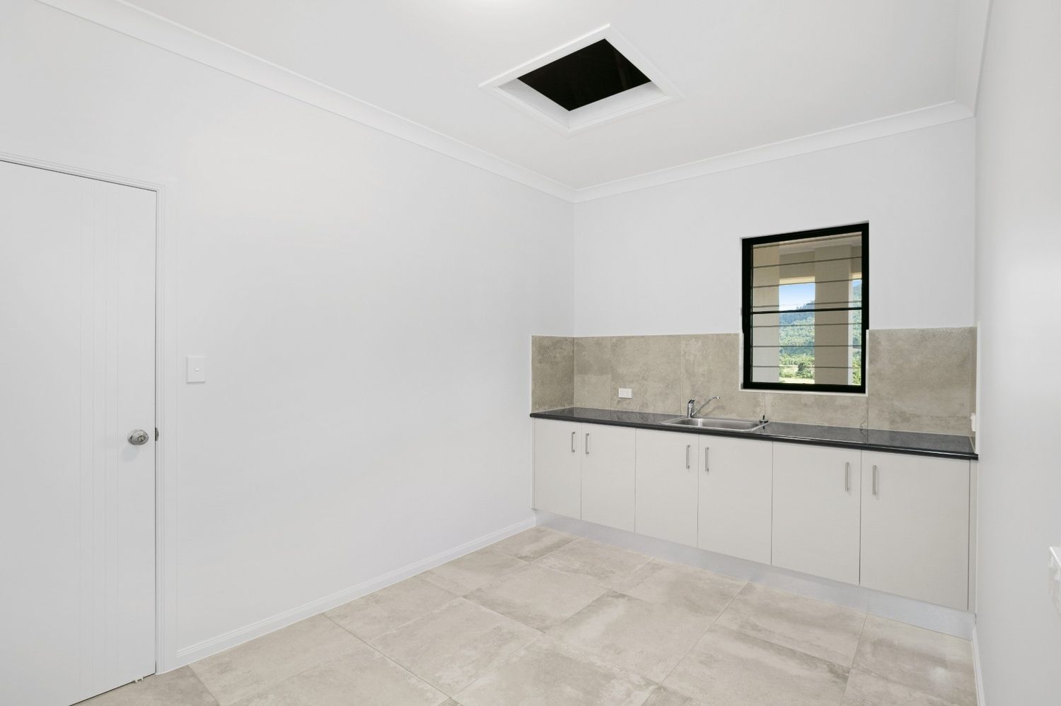 An Empty Kitchen With White Cabinets and a Window — Ashlee Jones Homes in Gordonvale, QLD