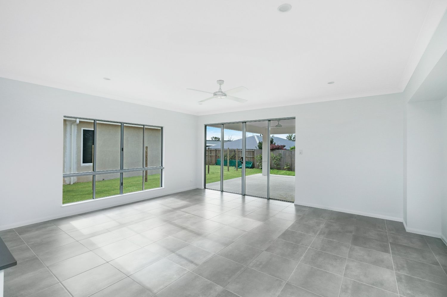 An Empty Living Room With Sliding Glass Doors and a Ceiling Fan — Ashlee Jones Homes in Gordonvale, QLD