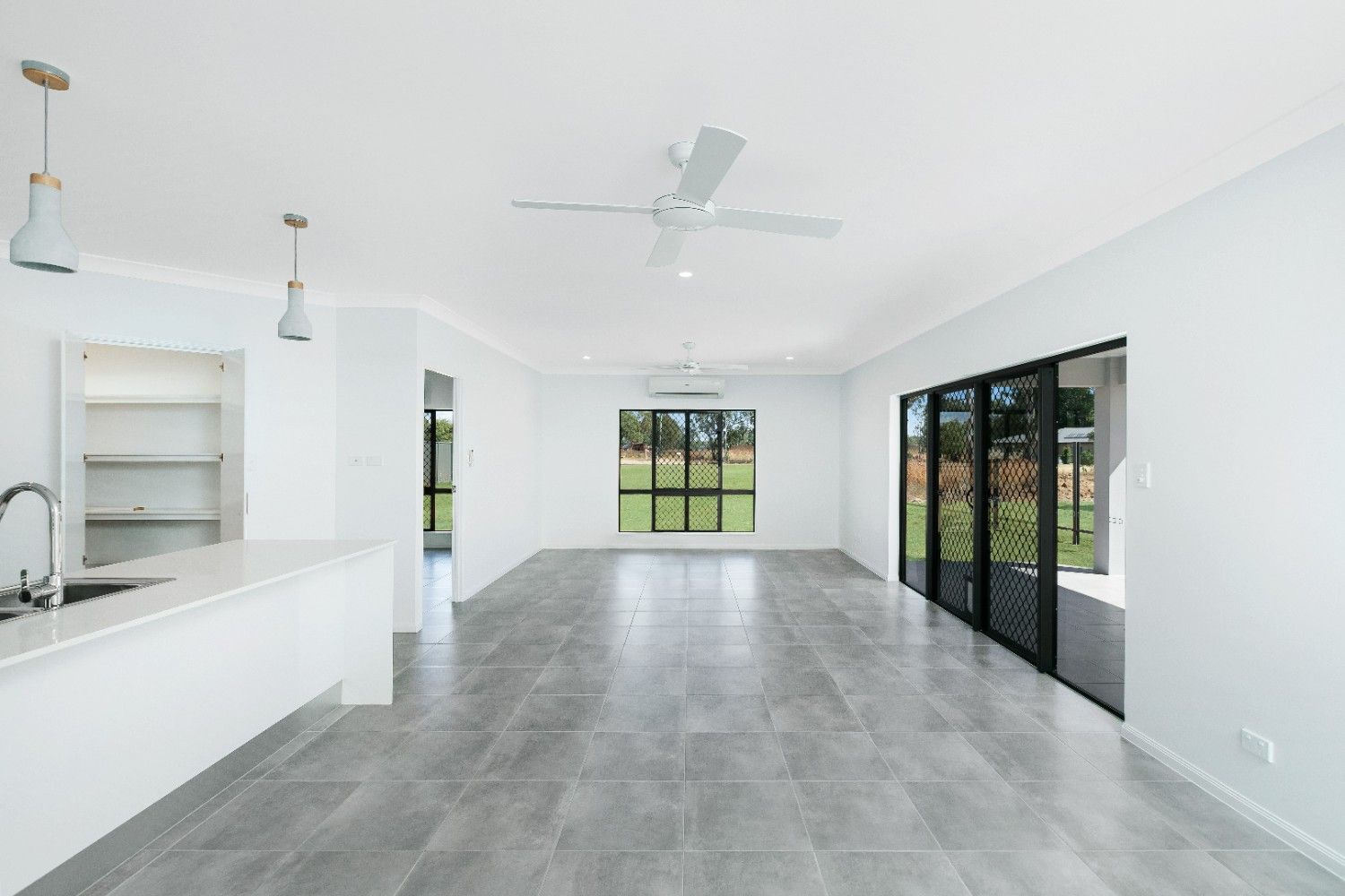 A Large Empty Room With a Ceiling Fan and Sliding Glass Doors — Ashlee Jones Homes in Gordonvale, QLD