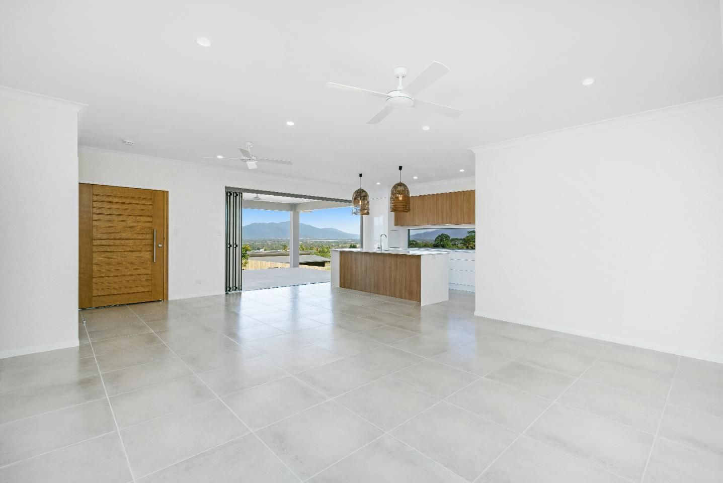 An Empty Living Room With a Ceiling Fan and a Kitchen in the Background — Ashlee Jones Homes in Gordonvale, QLD