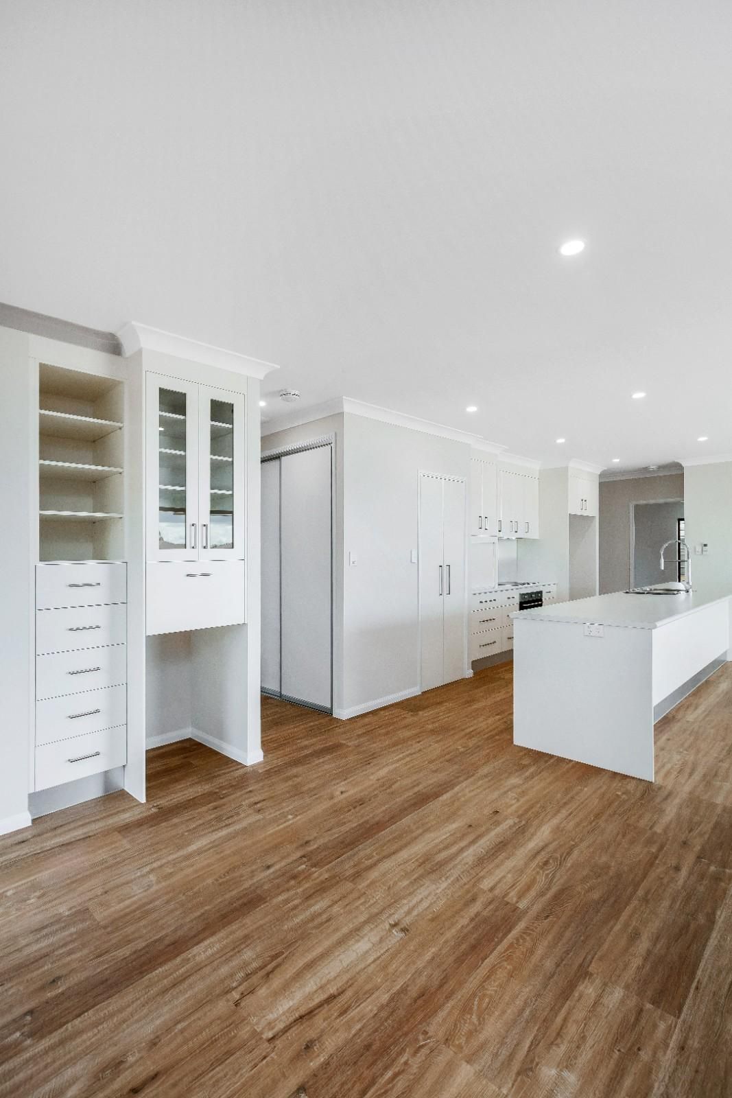 An Empty Kitchen With Hardwood Floors and White Cabinets — Ashlee Jones Homes in Gordonvale, QLD