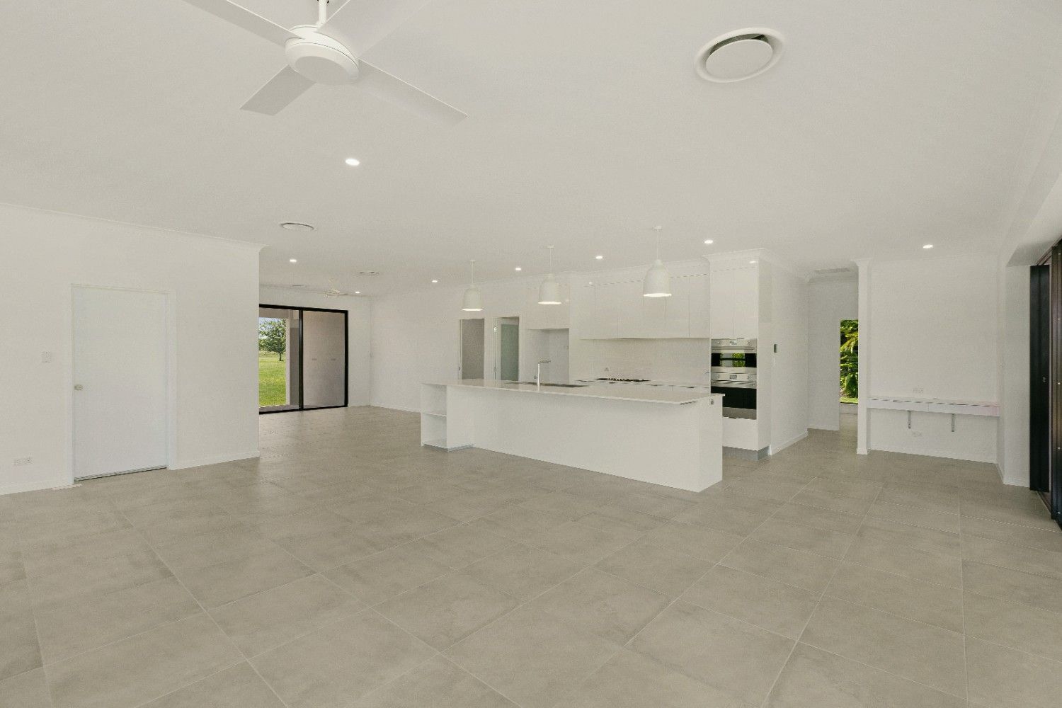 A Large Empty Room With a Ceiling Fan and a Kitchen — Ashlee Jones Homes in Gordonvale, QLD