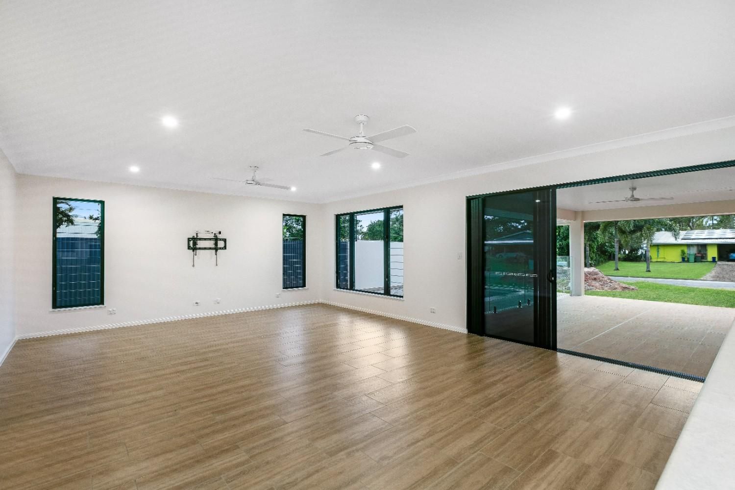 An Empty Living Room With Hardwood Floors and a Ceiling Fan — Ashlee Jones Homes in Gordonvale, QLD