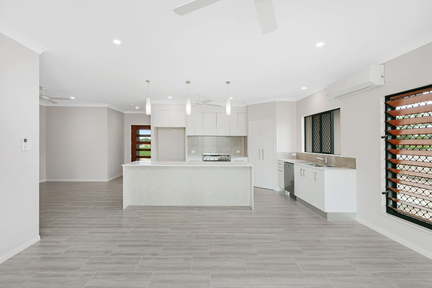 A Kitchen With White Cabinets, a Large Island, and a Ceiling Fan — Ashlee Jones Homes in Gordonvale, QLD