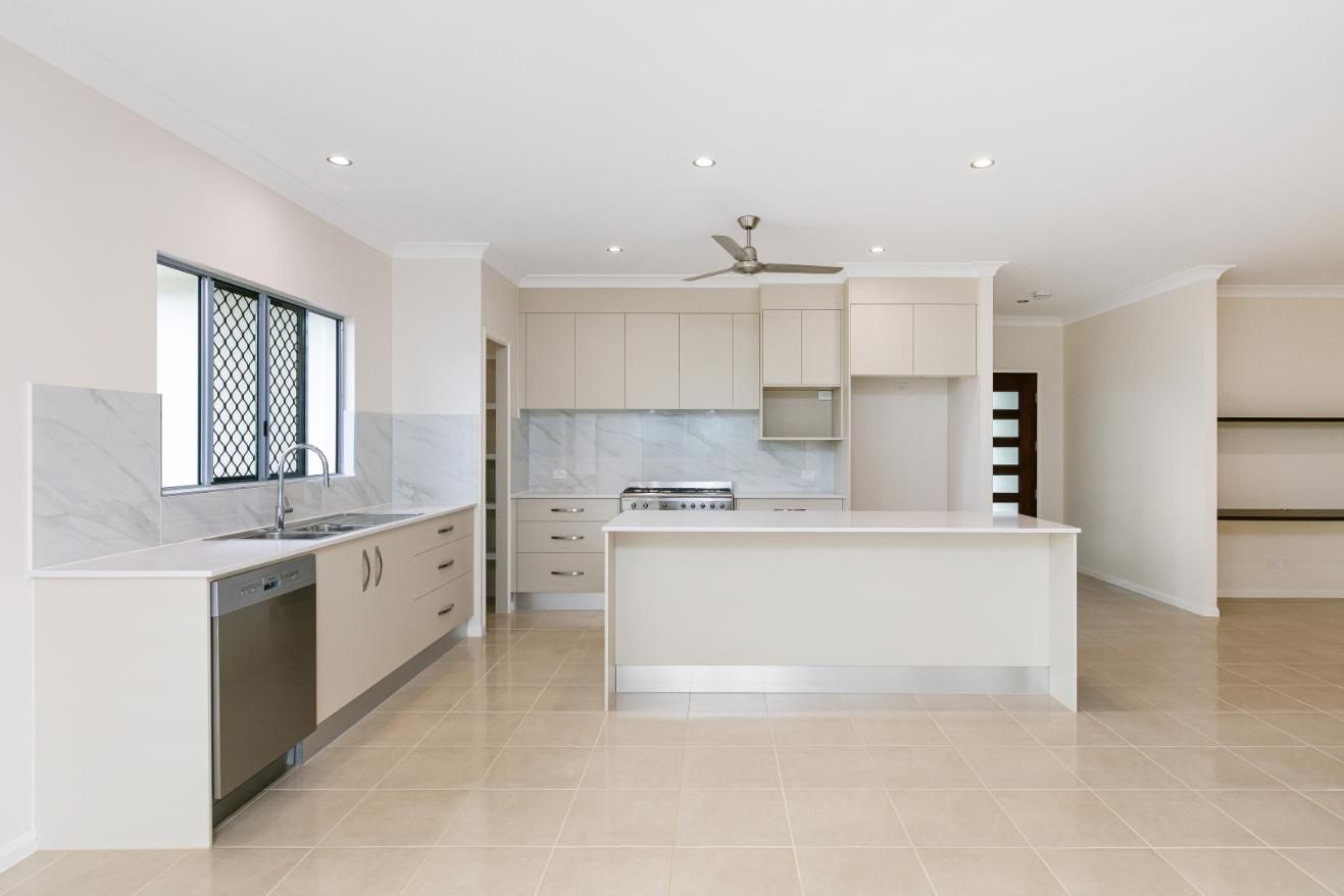 An Empty Kitchen With White Cabinets and a Large Island — Ashlee Jones Homes in Gordonvale, QLD