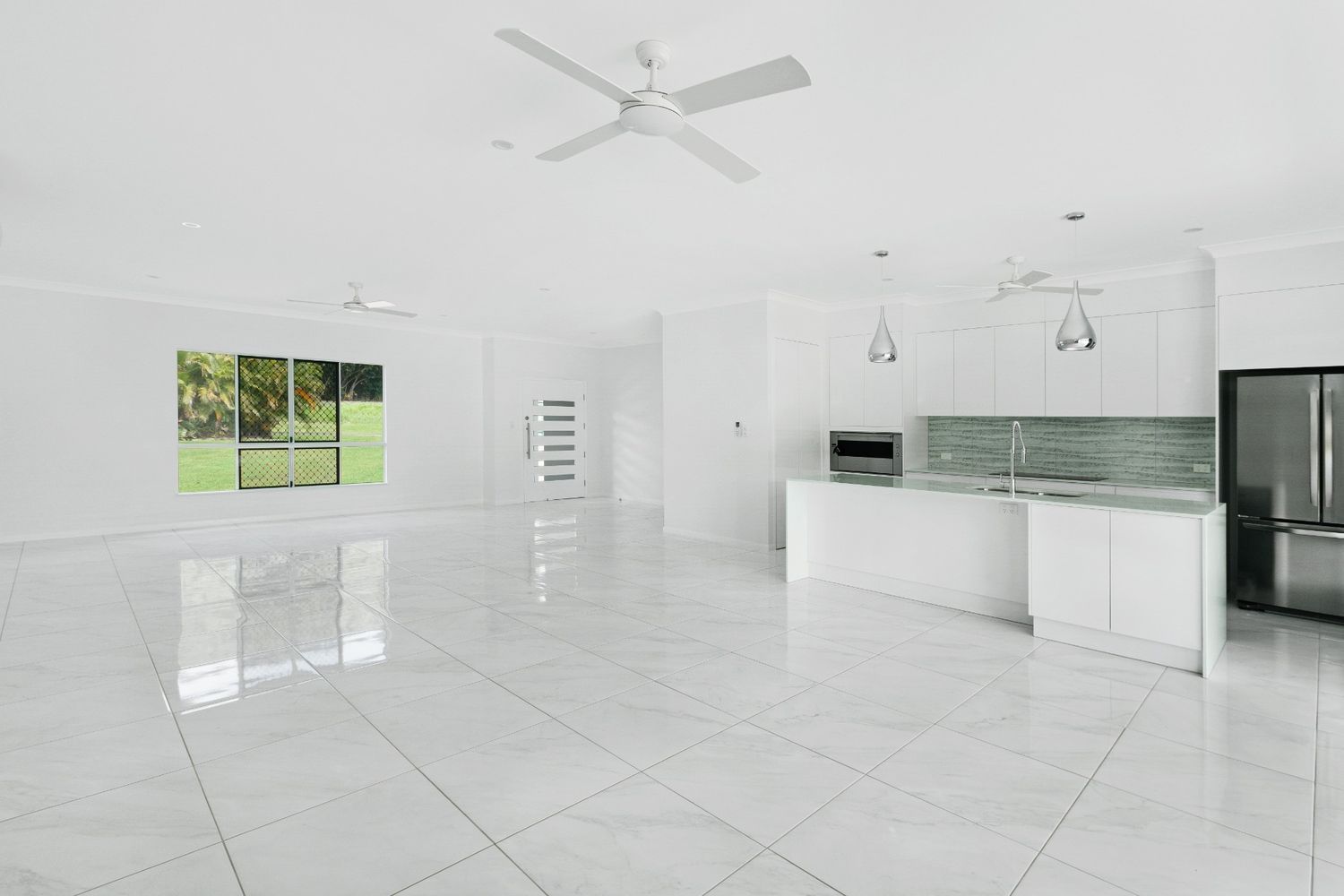 An Empty Kitchen With White Cabinets and a Ceiling Fan — Ashlee Jones Homes in Gordonvale, QLD
