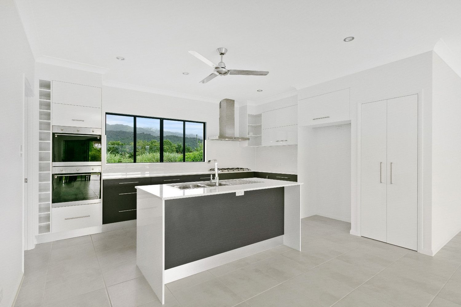 An Empty Kitchen With a Large Island and a Ceiling Fan — Ashlee Jones Homes in Gordonvale, QLD