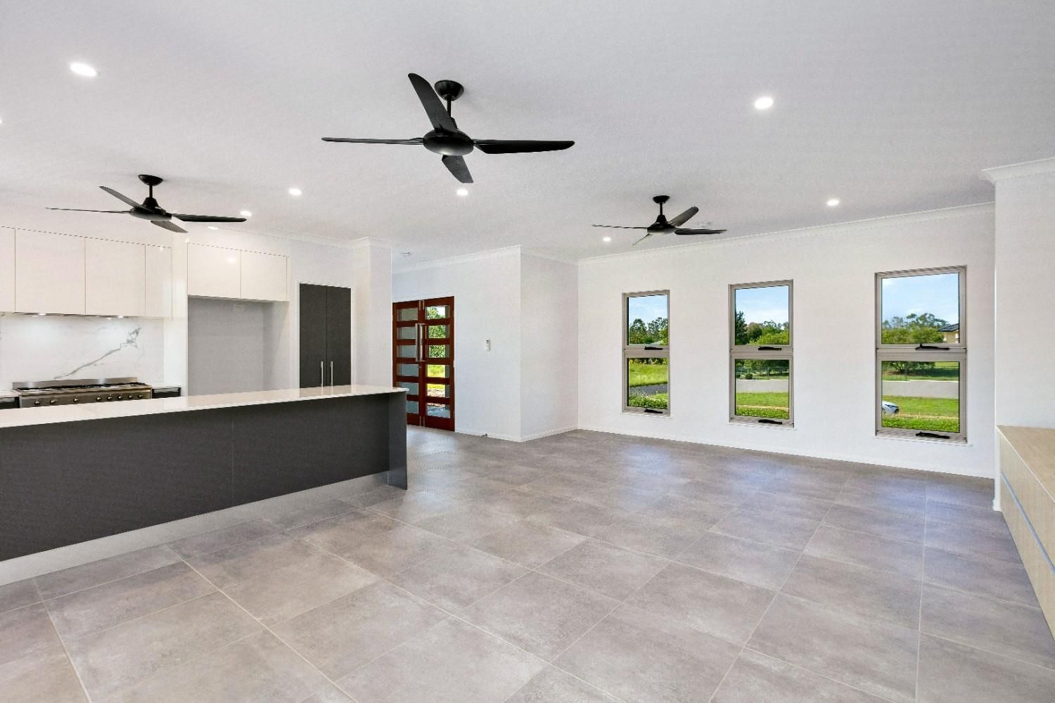A Large Empty Room With a Ceiling Fan and Three Windows — Ashlee Jones Homes in Gordonvale, QLD