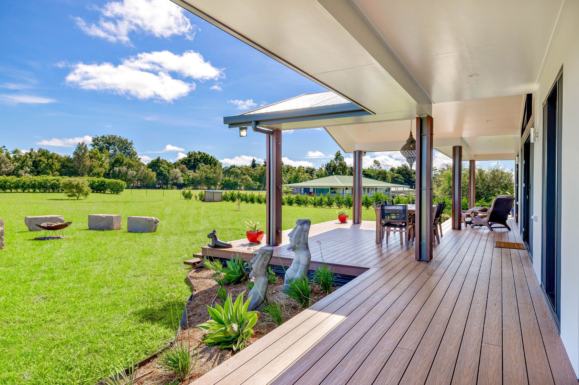A Wooden Deck With Patio Furniture Overlooks a Sprawling Green Lawn — Ashlee Jones Homes in Gordonvale, QLD