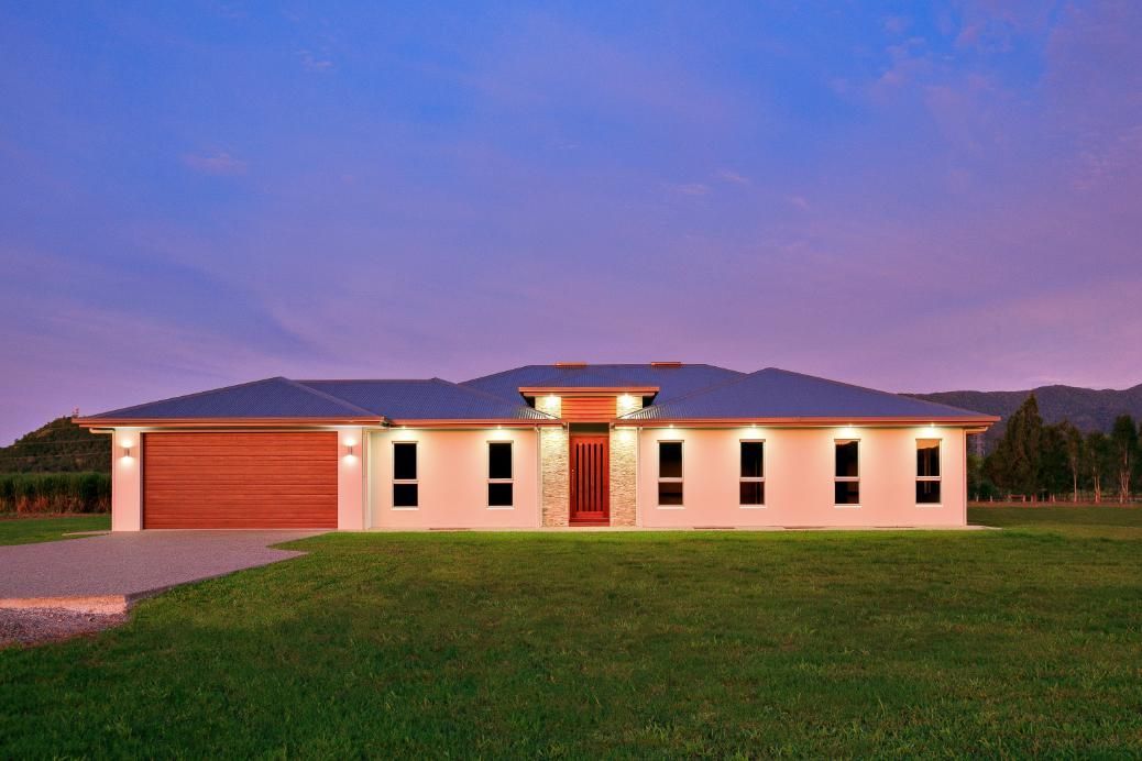 A Large White House With a Red Door is Sitting on Top of a Lush Green Field — Ashlee Jones Homes in Gordonvale, QLD