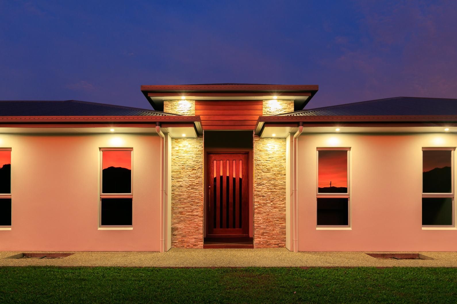 A House With a Red Door and Windows is Lit Up at Night — Ashlee Jones Homes in Gordonvale, QLD