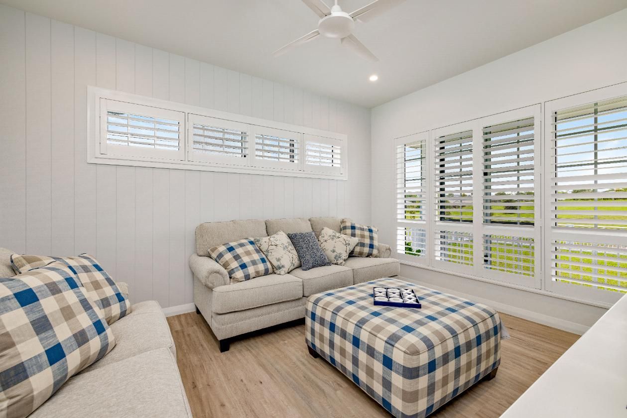 A Living Room With a Couch, Ottoman, and Shutters on the Windows — Ashlee Jones Homes in Gordonvale, QLD