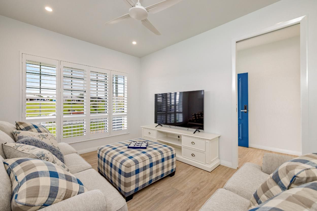 A Living Room With a Couch, Chairs, Ottoman and Television — Ashlee Jones Homes in Gordonvale, QLD