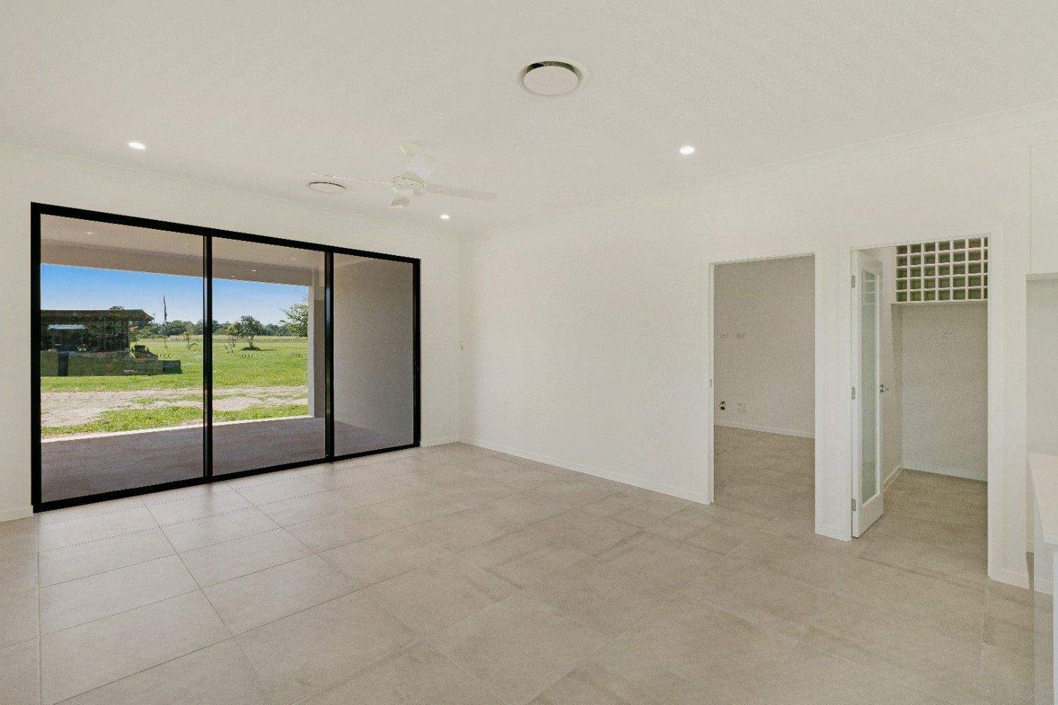 An Empty Room With Sliding Glass Doors and a View of a Field — Ashlee Jones Homes in Gordonvale, QLD