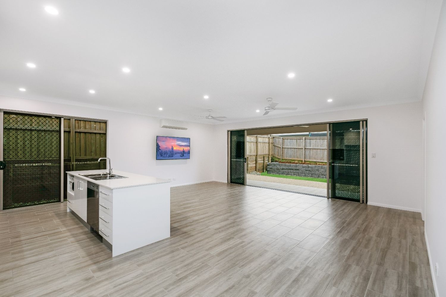 A Large Empty Room With a Kitchen and a Television on the Wall — Ashlee Jones Homes in Gordonvale, QLD