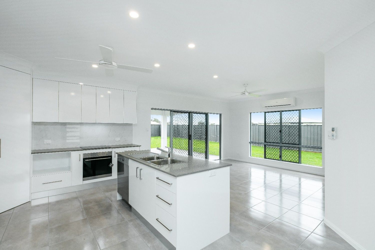 An Empty Kitchen With White Cabinets and a Large Island — Ashlee Jones Homes in Gordonvale, QLD