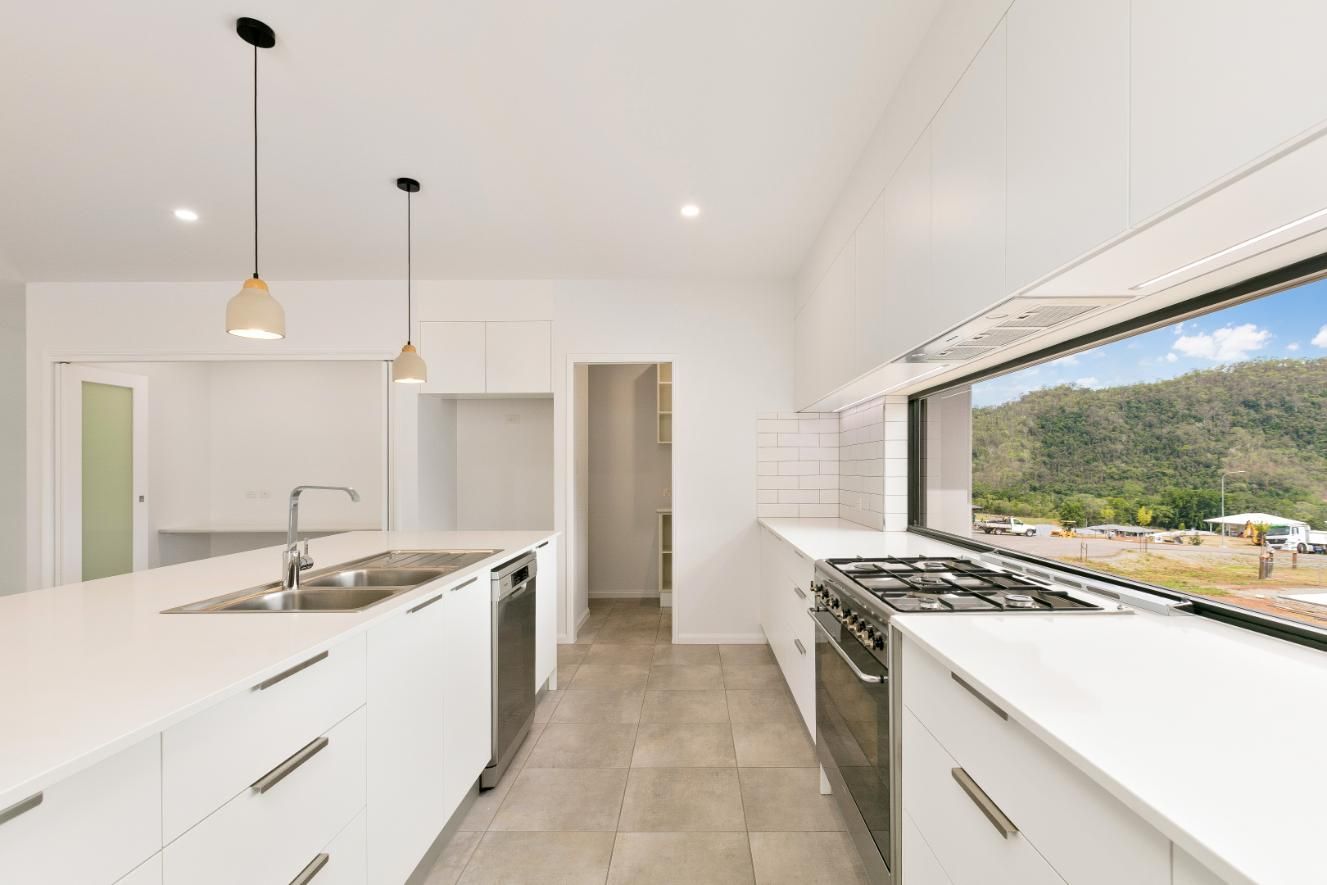 A Kitchen With White Cabinets and Stainless Steel Appliances and a Large Window — Ashlee Jones Homes in Gordonvale, QLD