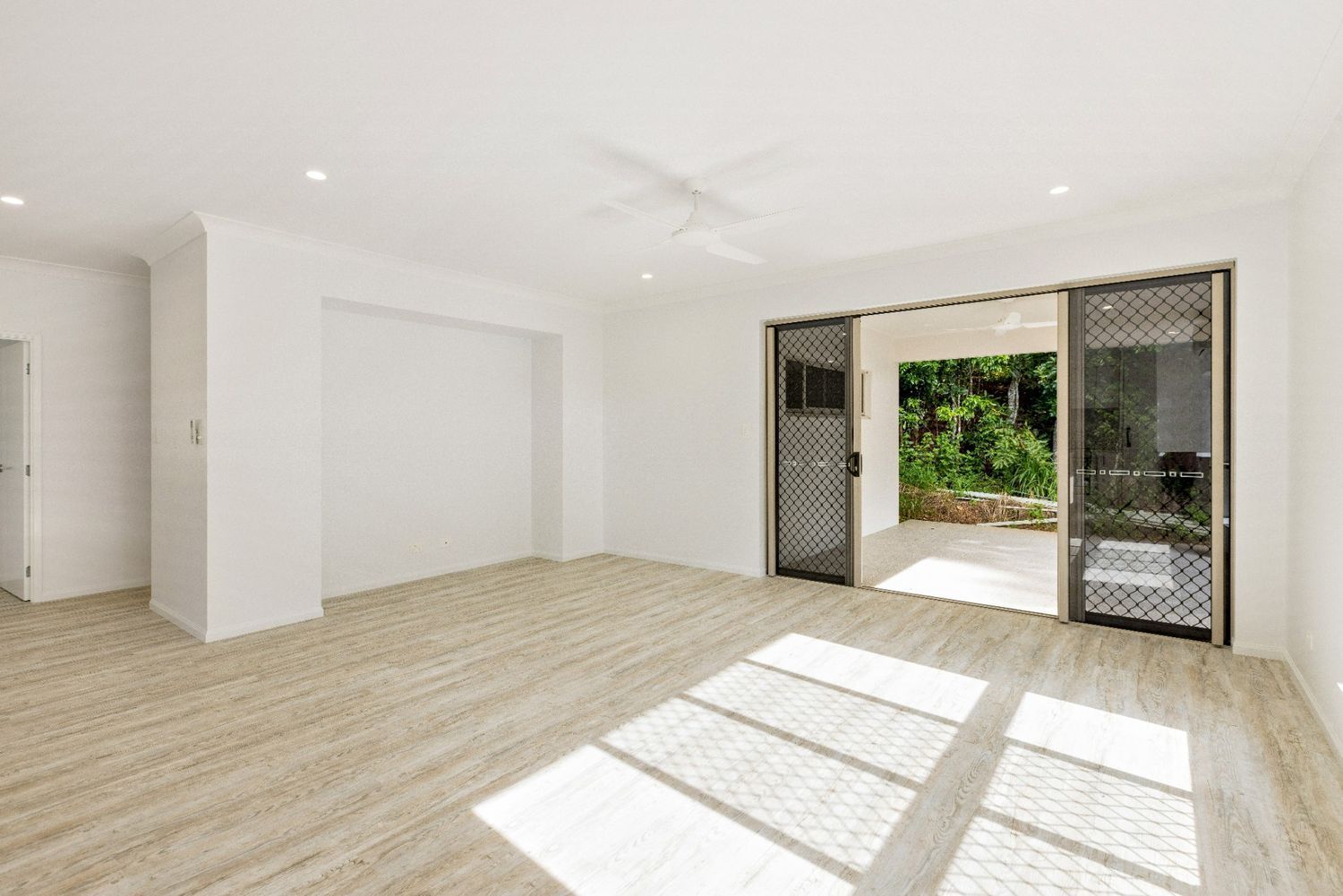 An Empty Living Room With Hardwood Floors and a Sliding Glass Door — Ashlee Jones Homes in Gordonvale, QLD