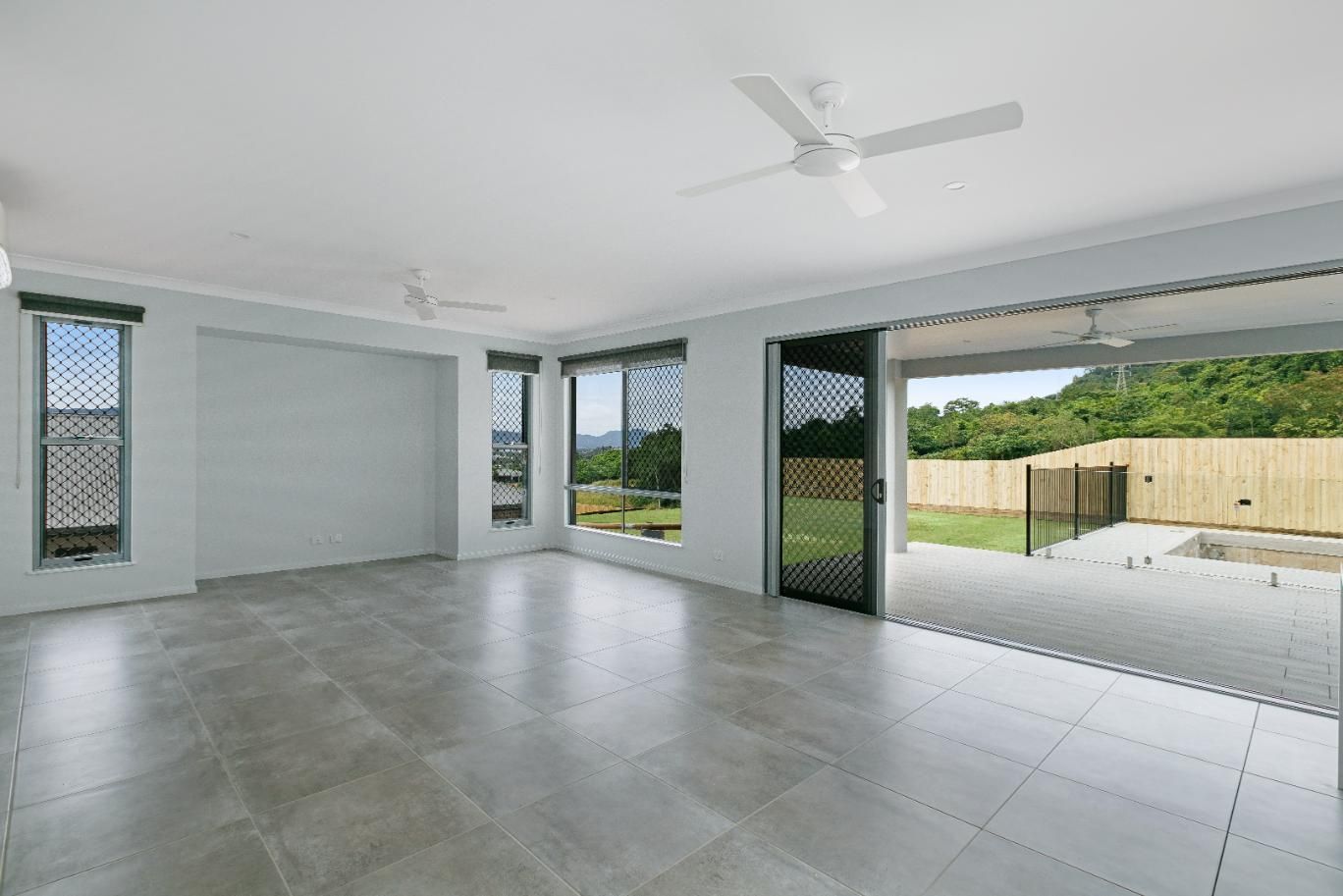 An Empty Living Room With a Ceiling Fan and Sliding Glass Doors Leading to a Patio — Ashlee Jones Homes in Gordonvale, QLD