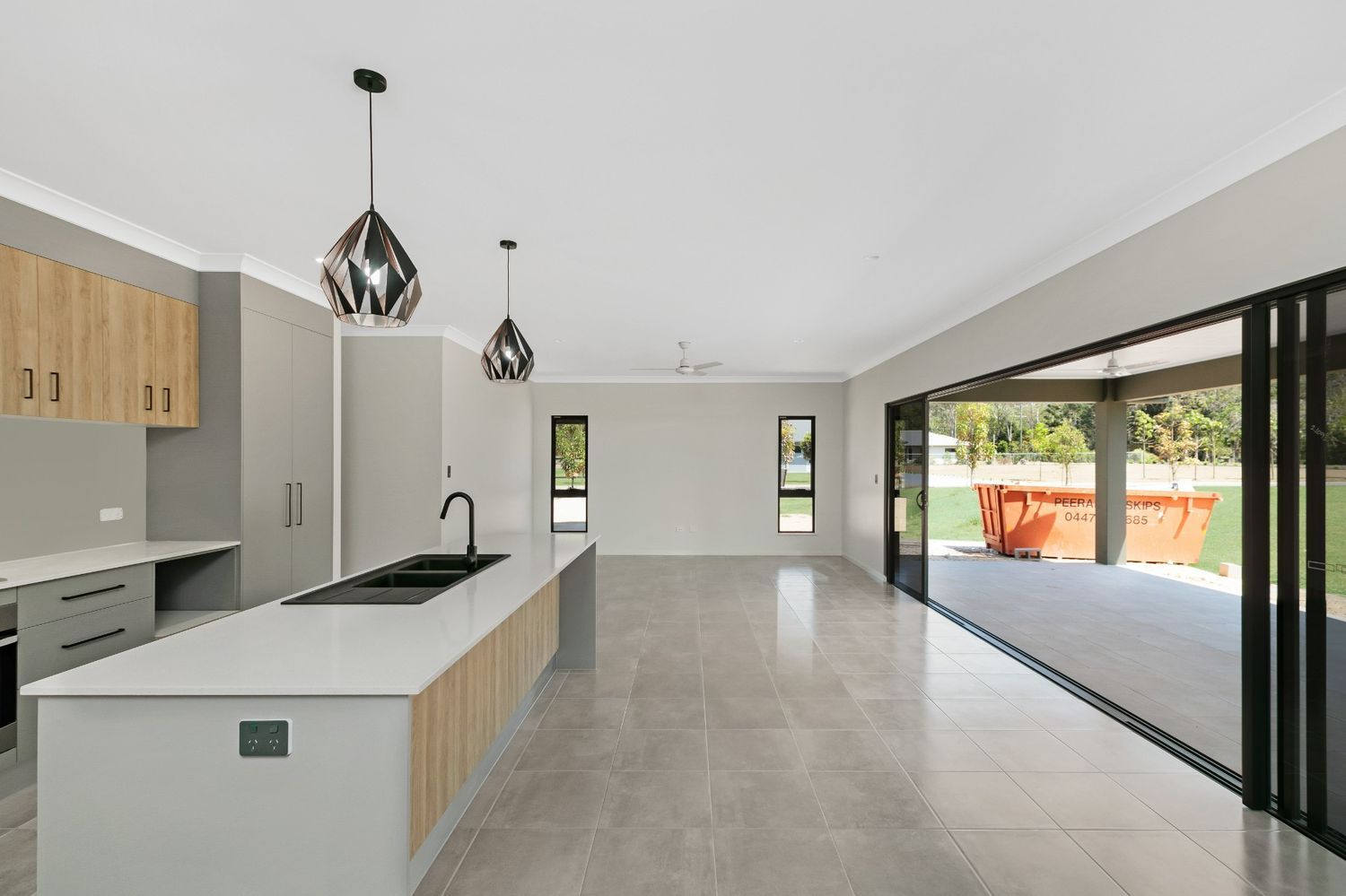 An Empty Kitchen With a Large Island and Sliding Glass Doors Leading to a Patio — Ashlee Jones Homes in Gordonvale, QLD