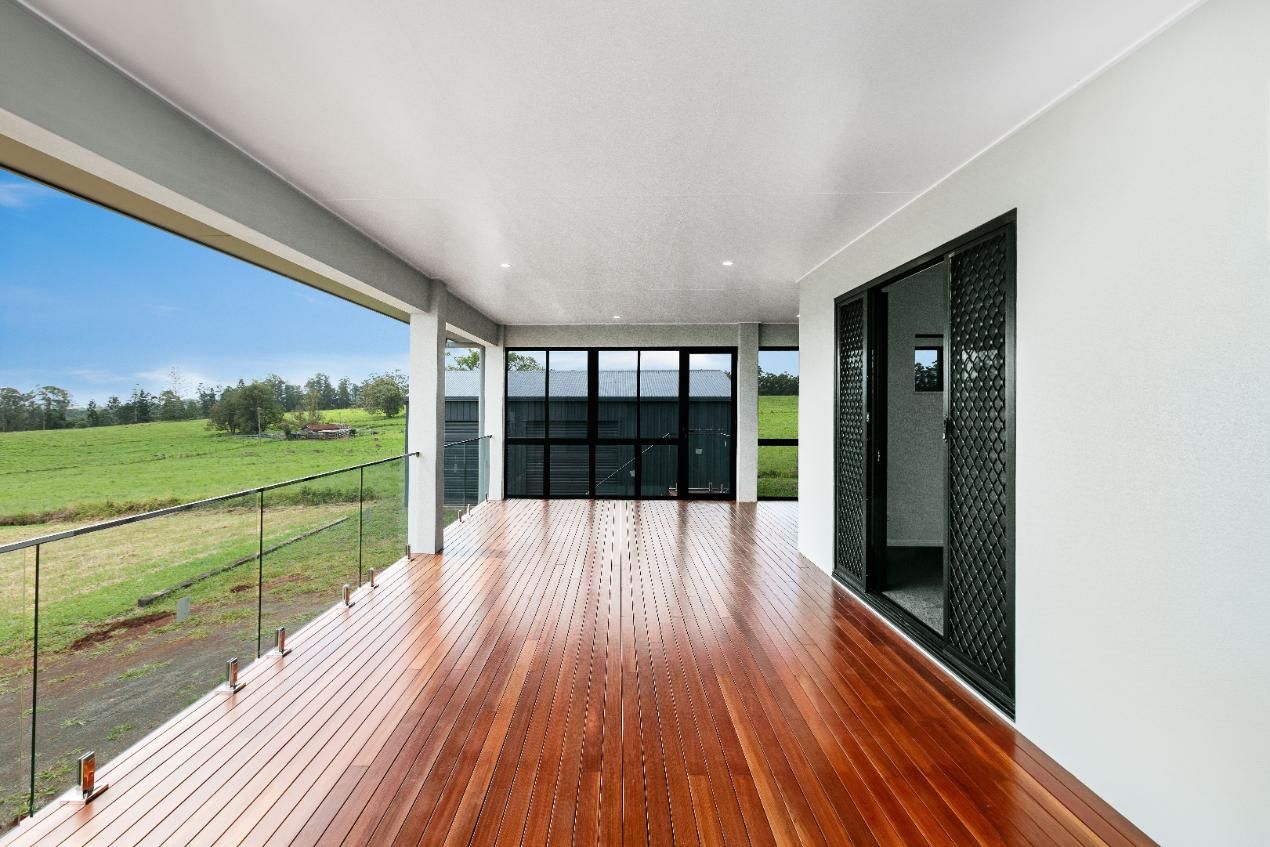 A Large Empty Room With a Wooden Floor and Lots of Windows — Ashlee Jones Homes in Gordonvale, QLD