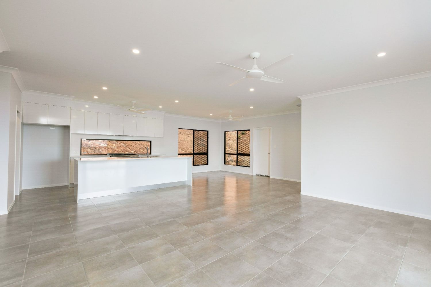 A Large Empty Room With a Ceiling Fan and a Kitchen in the Background — Ashlee Jones Homes in Gordonvale, QLD