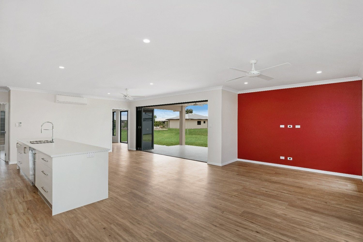 A Large Empty Room With Hardwood Floors and a Red Wall — Ashlee Jones Homes in Gordonvale, QLD