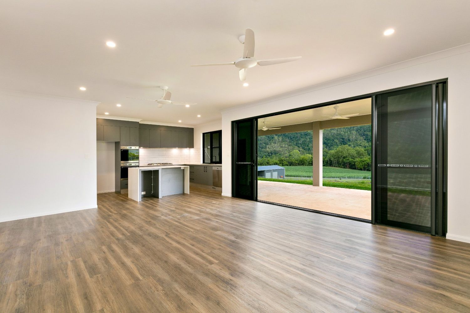 An Empty Living Room With Hardwood Floors and a Ceiling Fan — Ashlee Jones Homes in Gordonvale, QLD