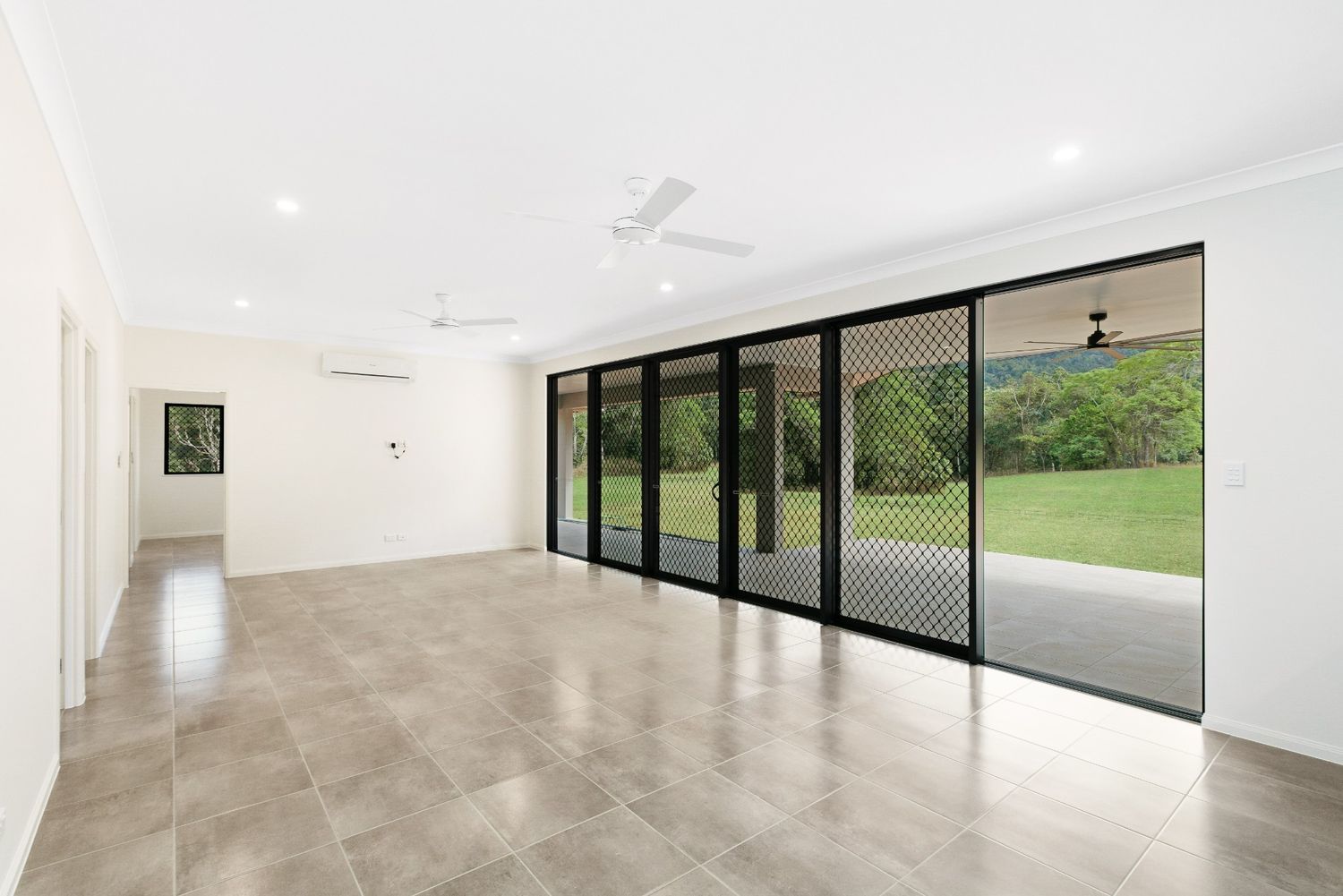An Empty Living Room With Sliding Glass Doors and a Ceiling Fan — Ashlee Jones Homes in Gordonvale, QLD