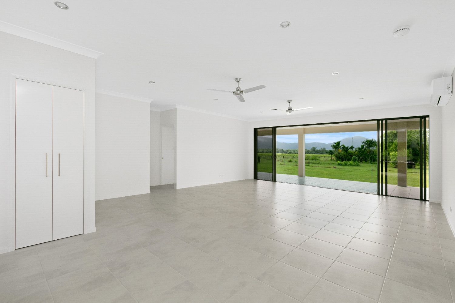 A Large Empty Room With a Ceiling Fan and Sliding Glass Doors — Ashlee Jones Homes in Gordonvale, QLD