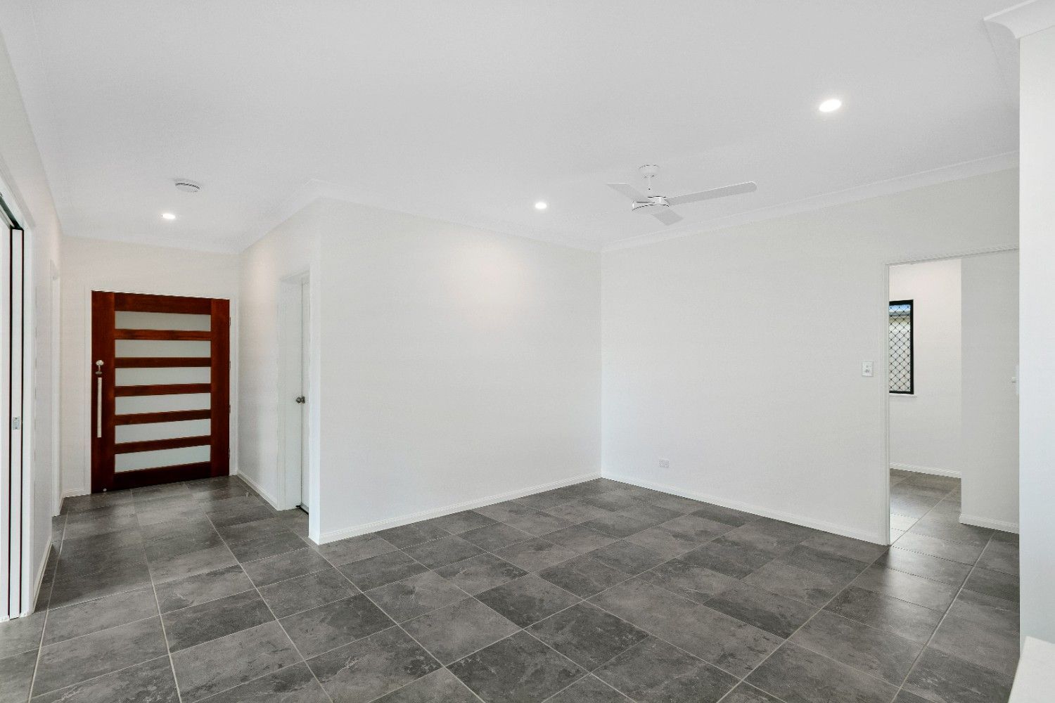 An Empty Living Room With a Tiled Floor and a Wooden Door — Ashlee Jones Homes in Gordonvale, QLD