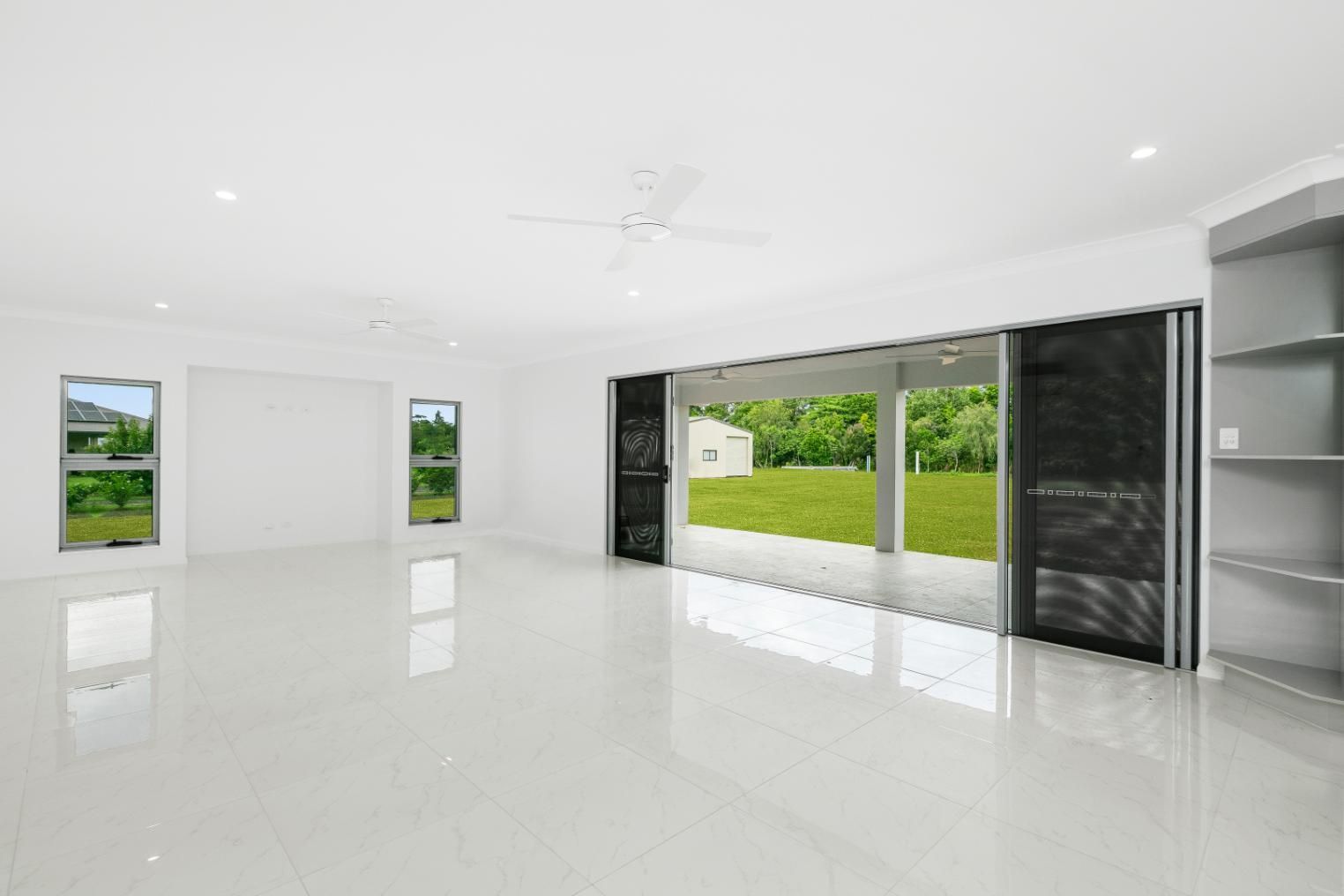 An Empty Living Room With Sliding Glass Doors and a Ceiling Fan — Ashlee Jones Homes in Gordonvale, QLD