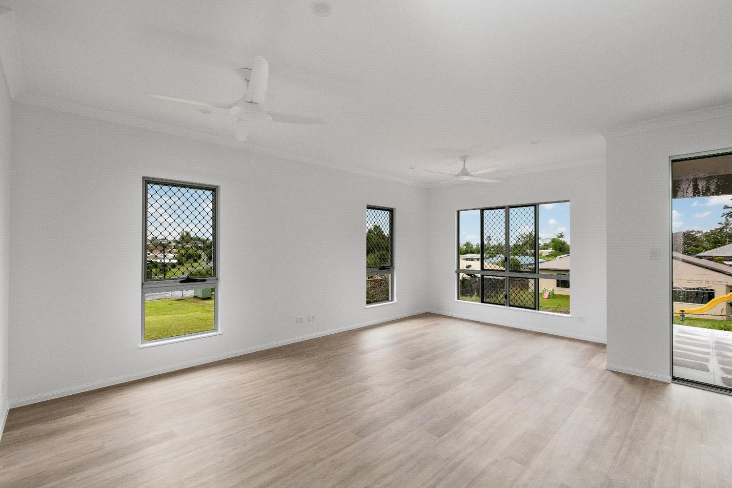 An Empty Living Room With Hardwood Floors and a Ceiling Fan — Ashlee Jones Homes in Gordonvale, QLD