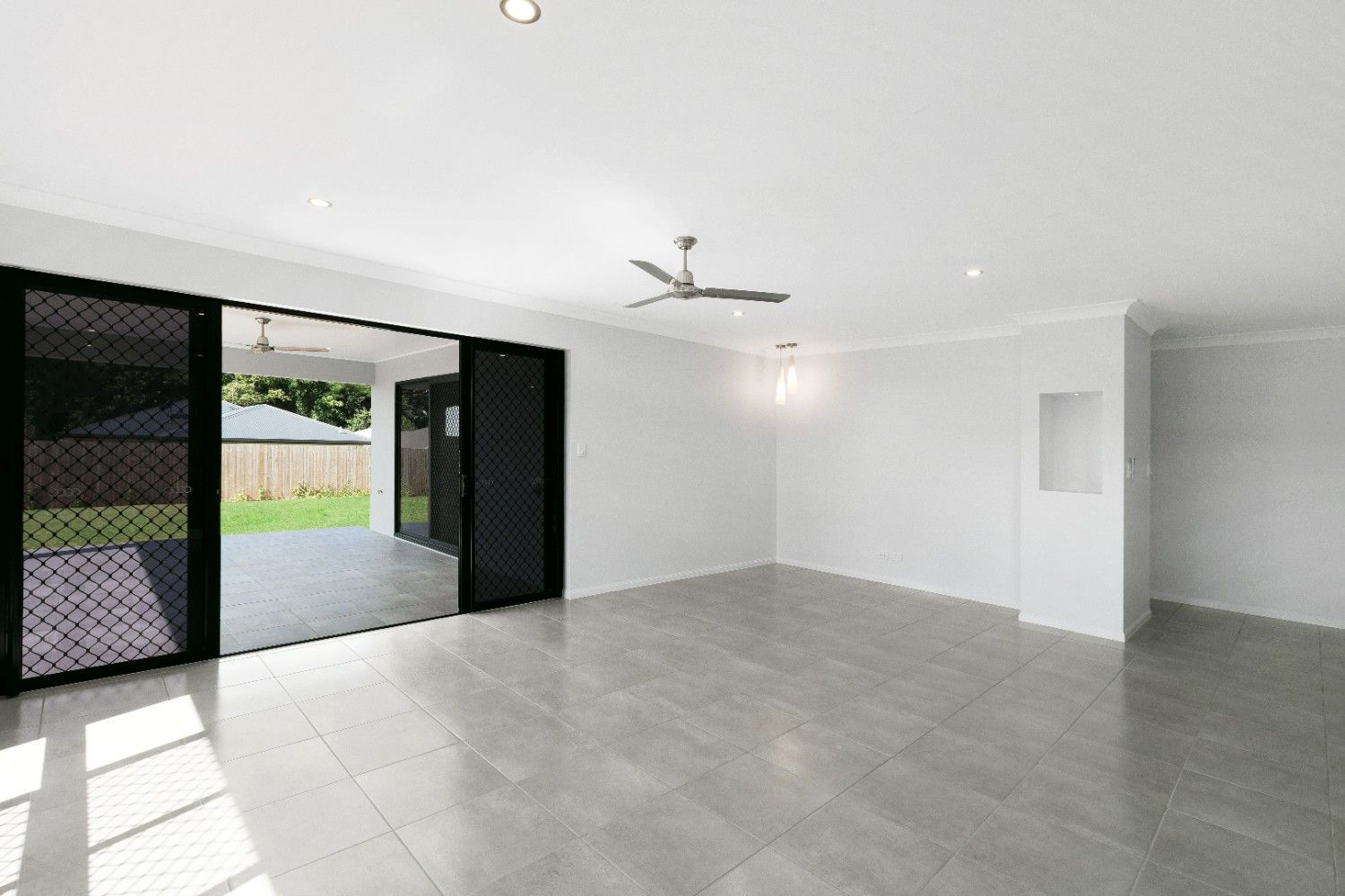 An Empty Living Room With a Ceiling Fan and Sliding Glass Doors Leading to a Patio — Ashlee Jones Homes in Gordonvale, QLD