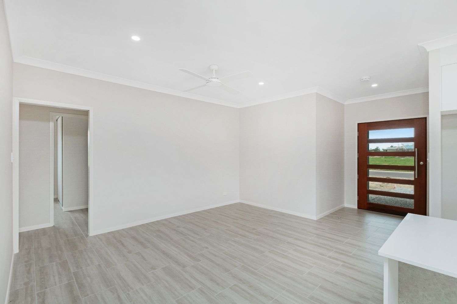 An Empty Living Room With Hardwood Floors and a Wooden Door — Ashlee Jones Homes in Gordonvale, QLD