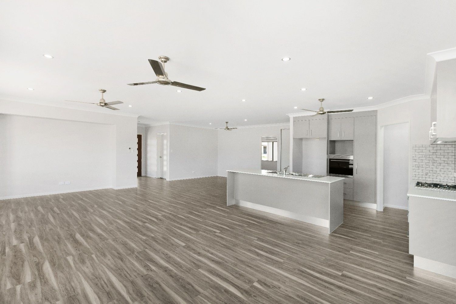 A Large Empty Room With Hardwood Floors and Ceiling Fans — Ashlee Jones Homes in Gordonvale, QLD