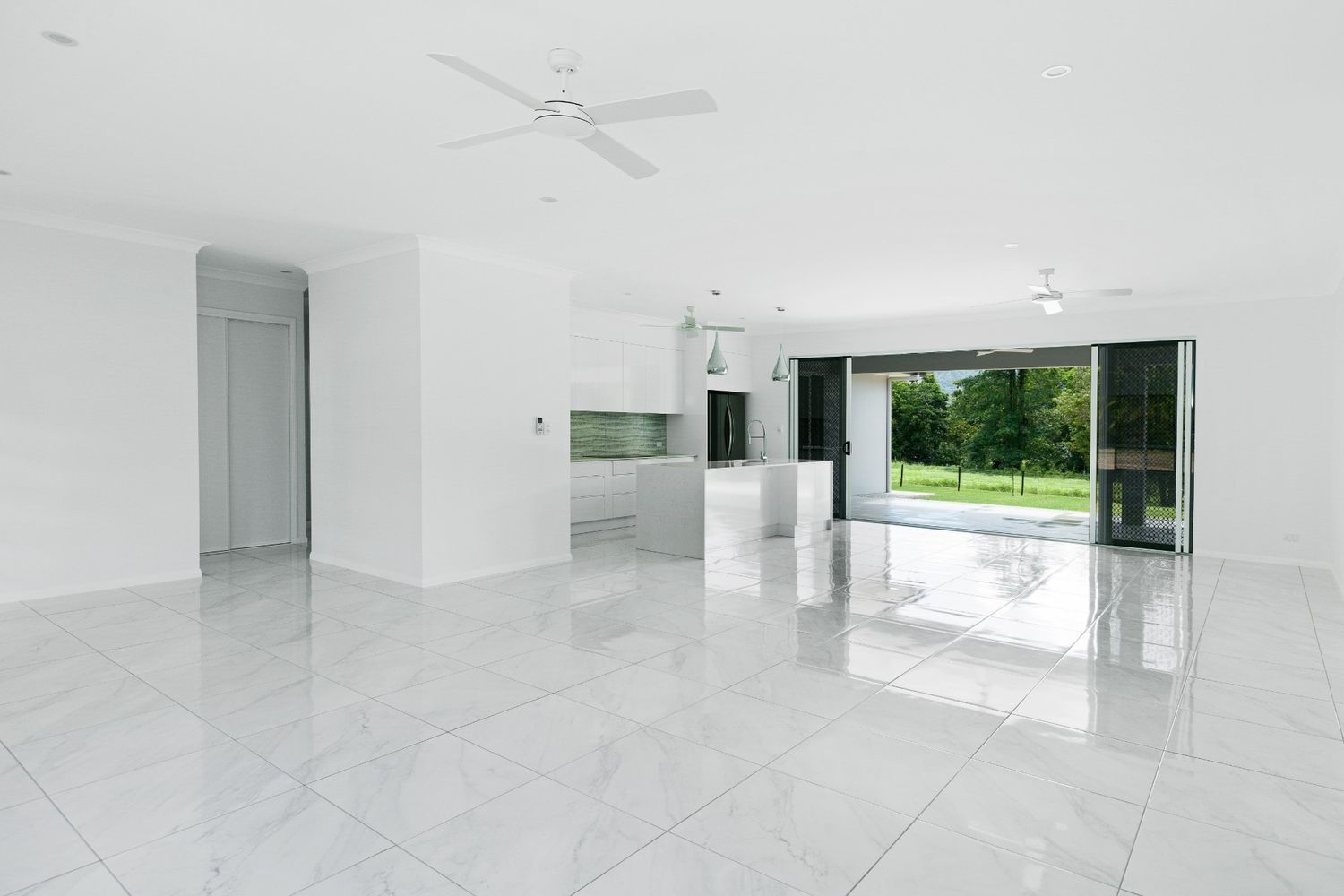 A Large Empty Room With White Tile Floors and a Ceiling Fan — Ashlee Jones Homes in Gordonvale, QLD