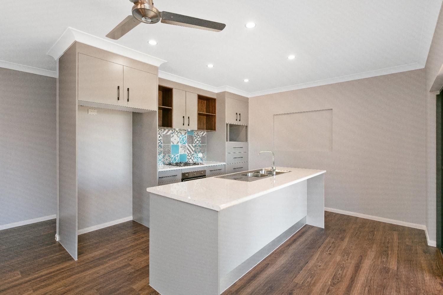 An Empty Kitchen With a Large Island and a Ceiling Fan — Ashlee Jones Homes in Gordonvale, QLD