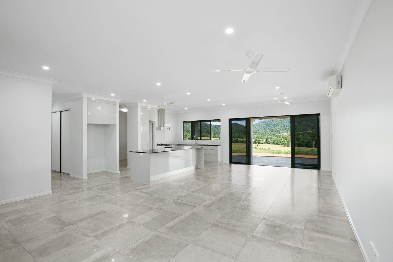 A Large Empty Room With a Kitchen and Sliding Glass Doors — Ashlee Jones Homes in Gordonvale, QLD