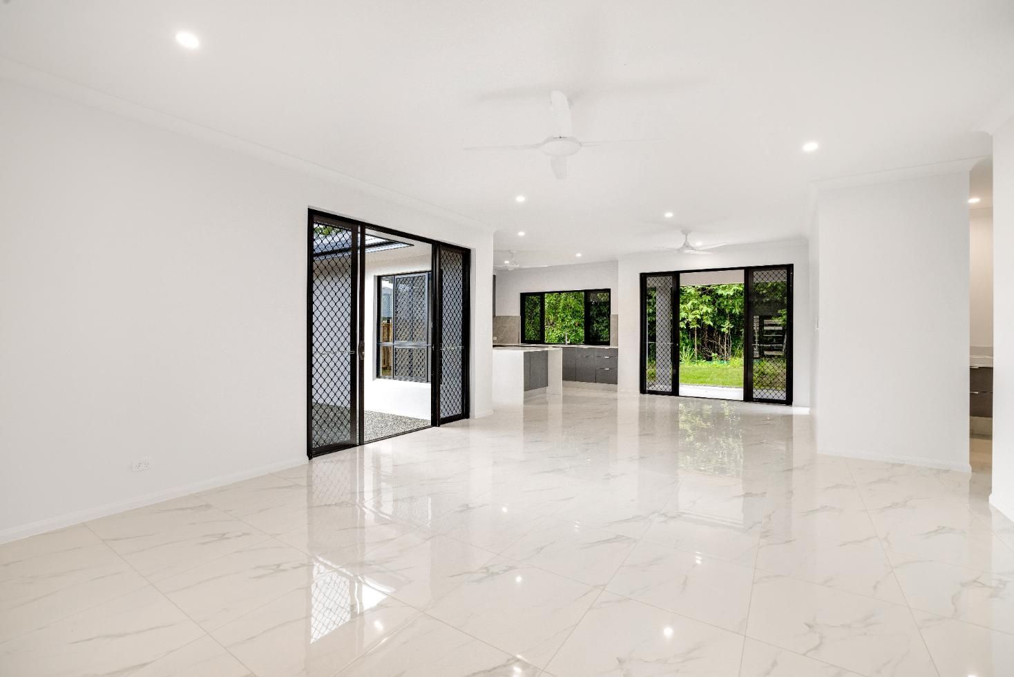 A Large Empty Room With Marble Floors and Sliding Glass Doors — Ashlee Jones Homes in Gordonvale, QLD