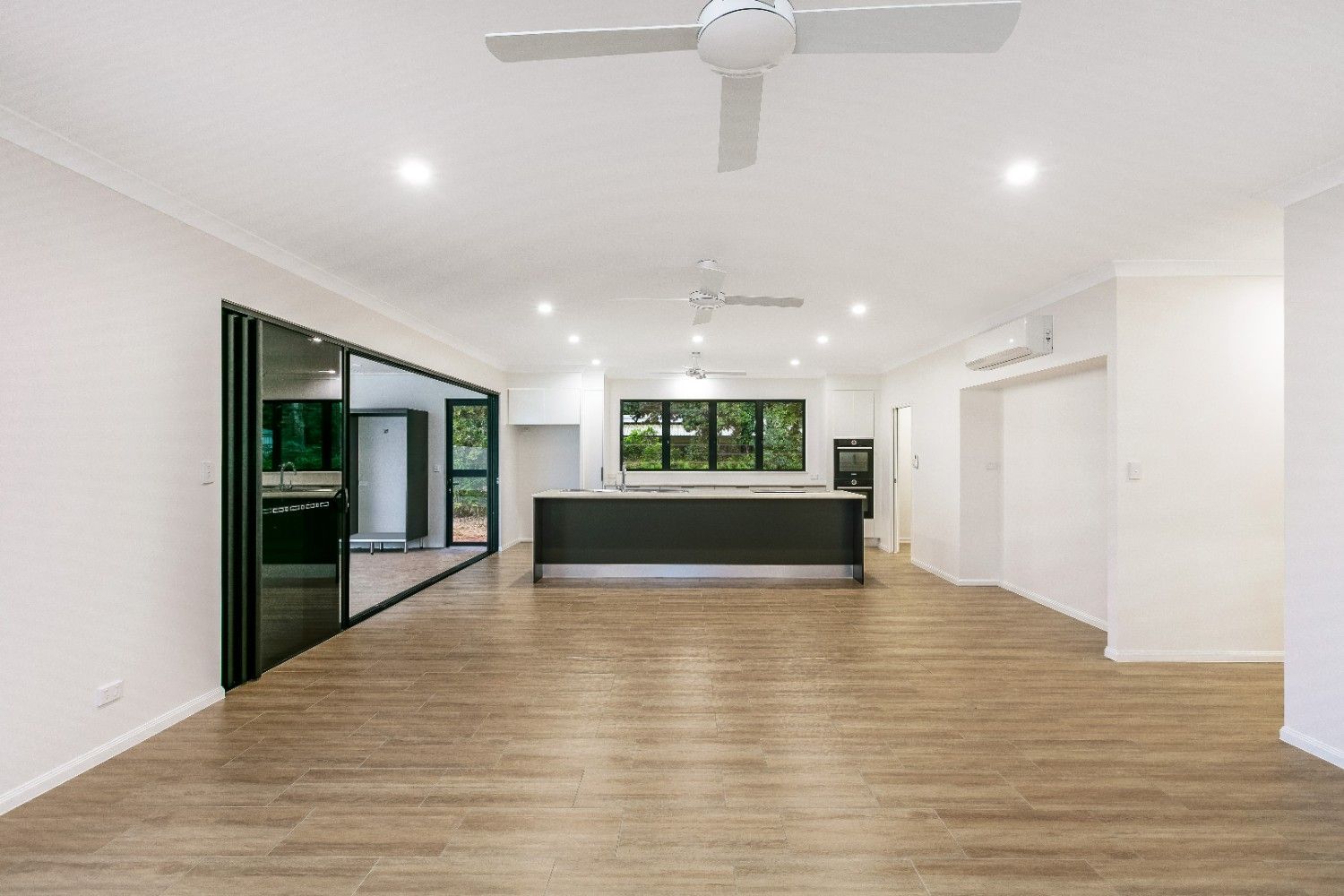A Large Empty Room With Hardwood Floors and a Ceiling Fan — Ashlee Jones Homes in Gordonvale, QLD