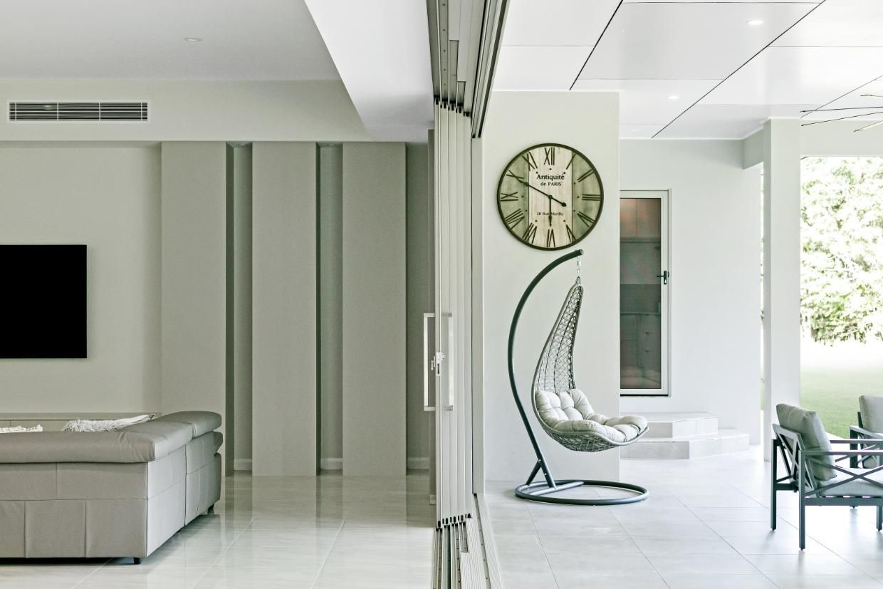 A Living Room With a Clock on the Wall and a Hanging Chair — Ashlee Jones Homes in Gordonvale, QLD