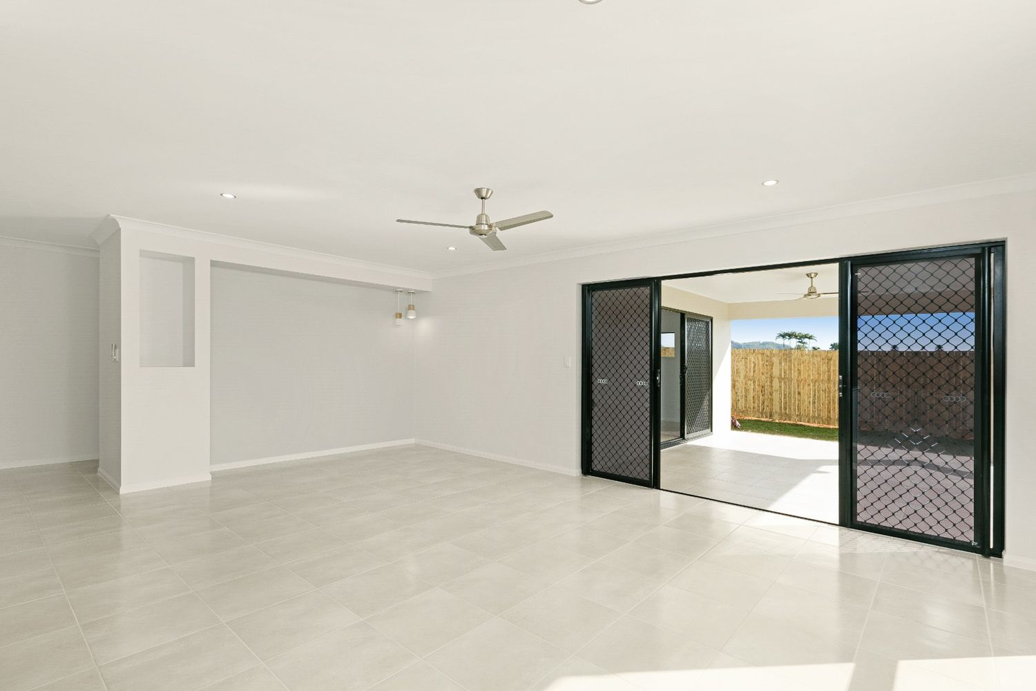 An Empty Living Room With Sliding Glass Doors and a Ceiling Fan — Ashlee Jones Homes in Gordonvale, QLD