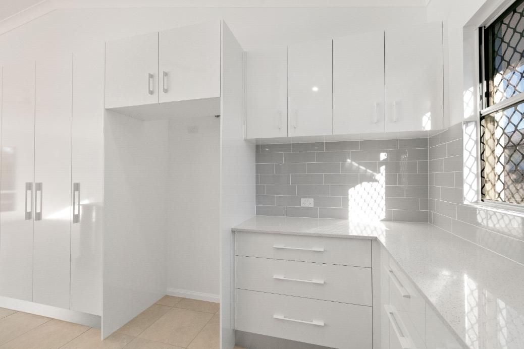 An Empty Kitchen With White Cabinets and a Window — Ashlee Jones Homes in Gordonvale, QLD