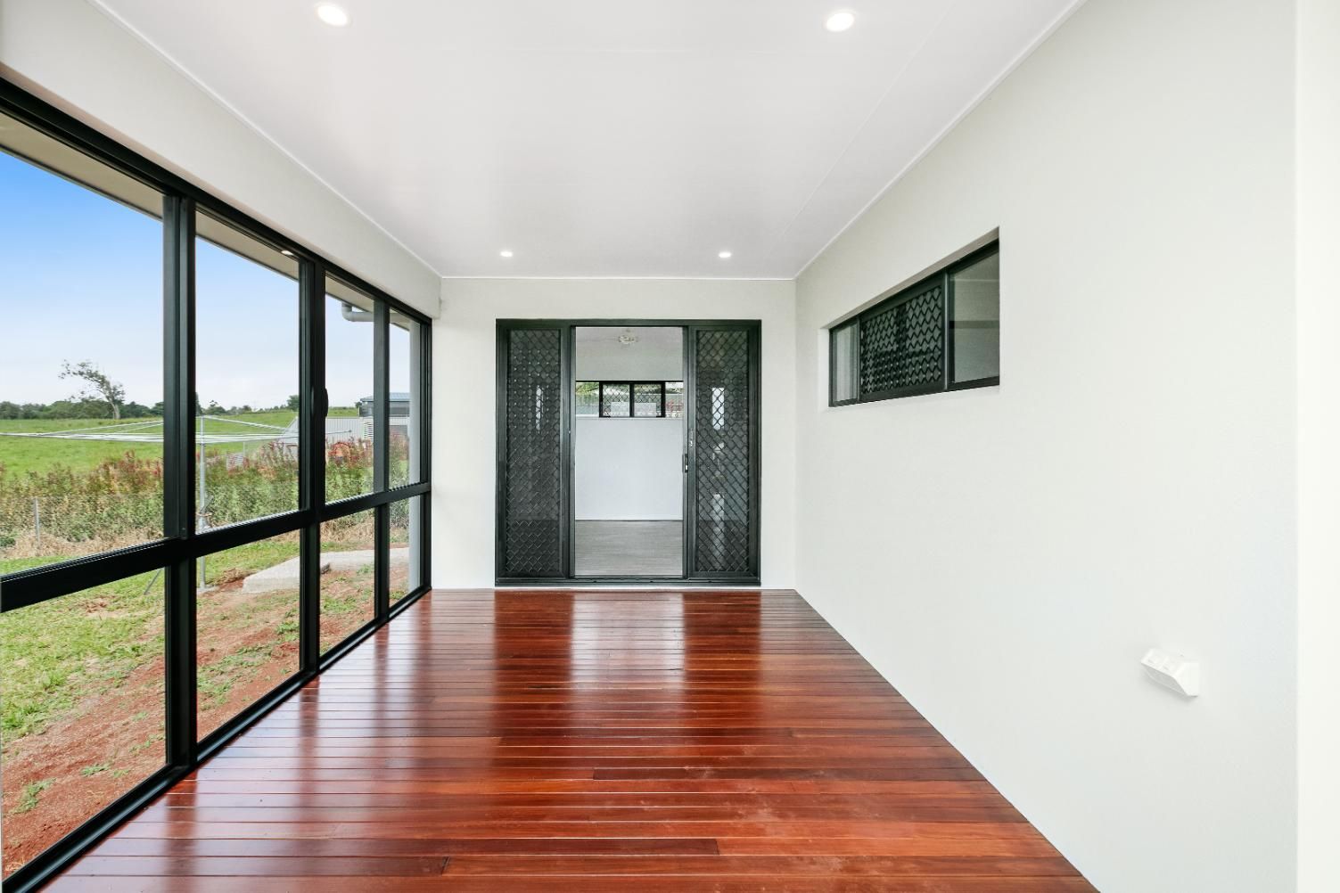 An Empty Room With Hardwood Floors and Lots of Windows — Ashlee Jones Homes in Gordonvale, QLD