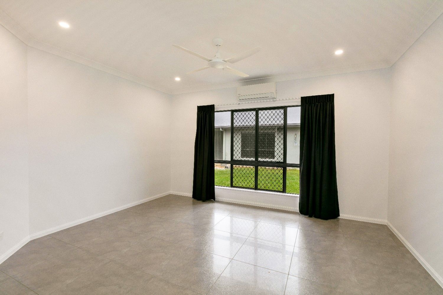 An Empty Living Room With a Large Window and Black Curtains — Ashlee Jones Homes in Gordonvale, QLD