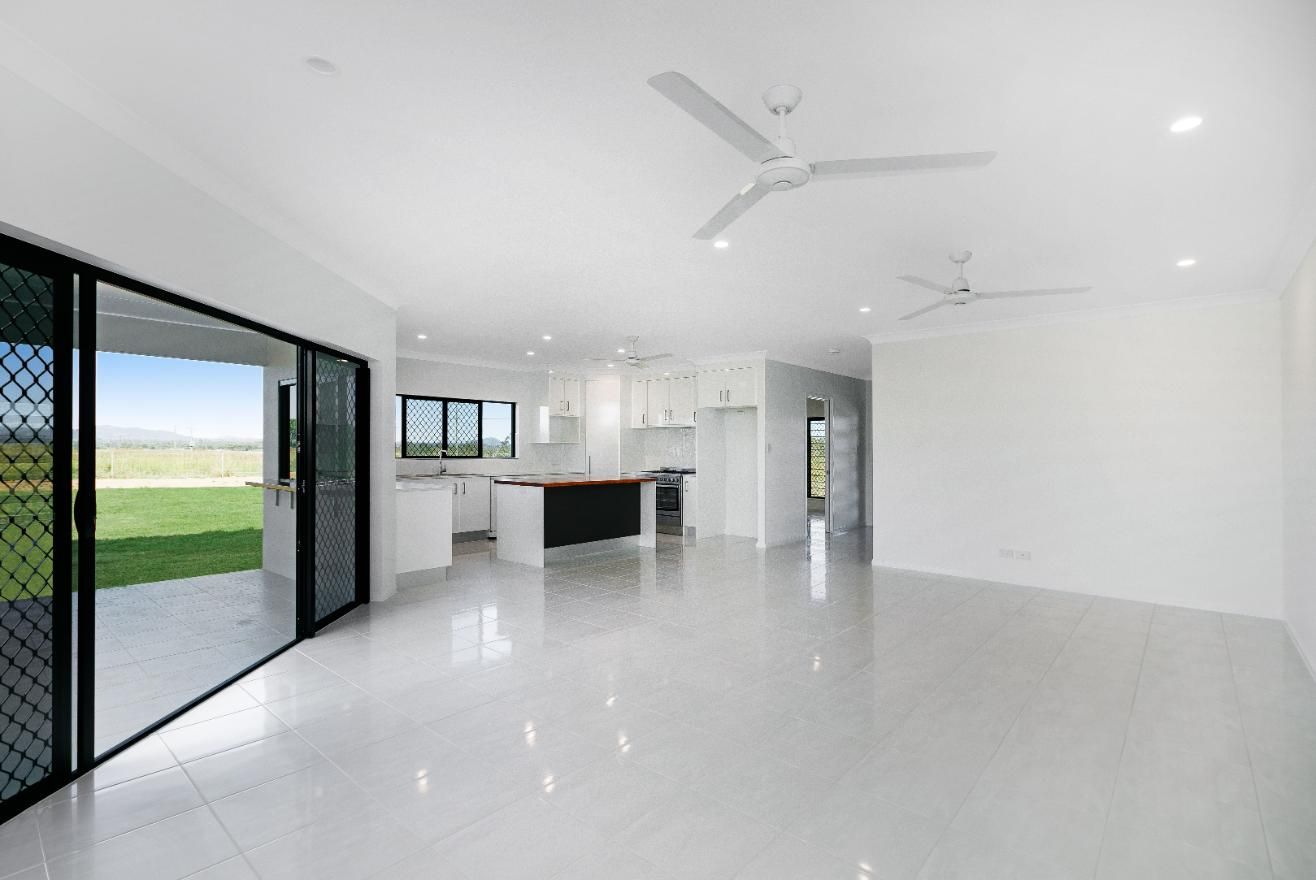 A Large Empty Room With a Ceiling Fan and Sliding Glass Doors Leading to a Kitchen — Ashlee Jones Homes in Gordonvale, QLD