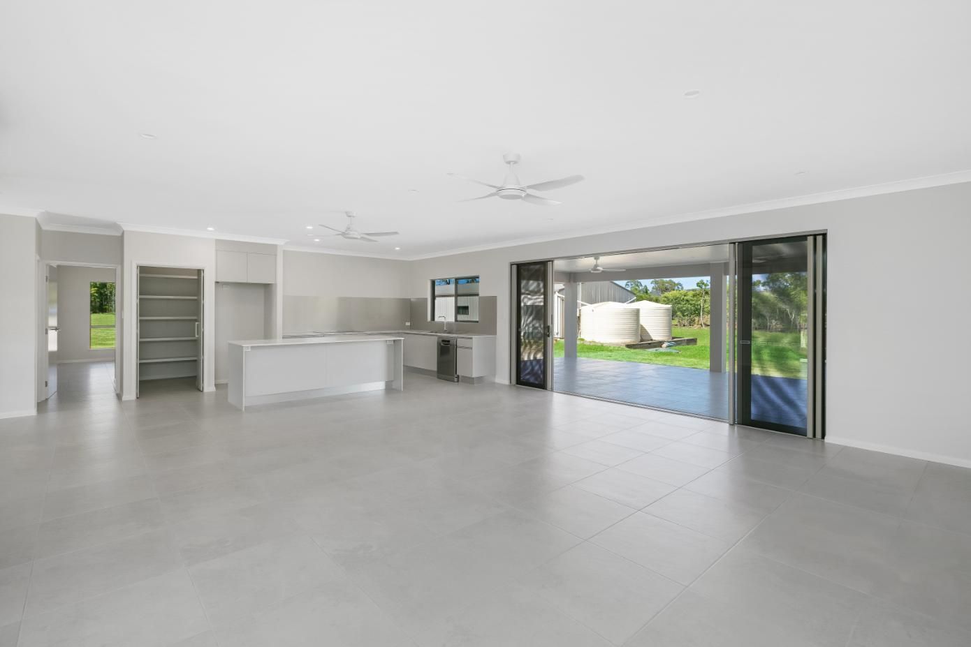 An Empty Living Room in a House With a Kitchen and Sliding Glass Doors — Ashlee Jones Homes in Gordonvale, QLD
