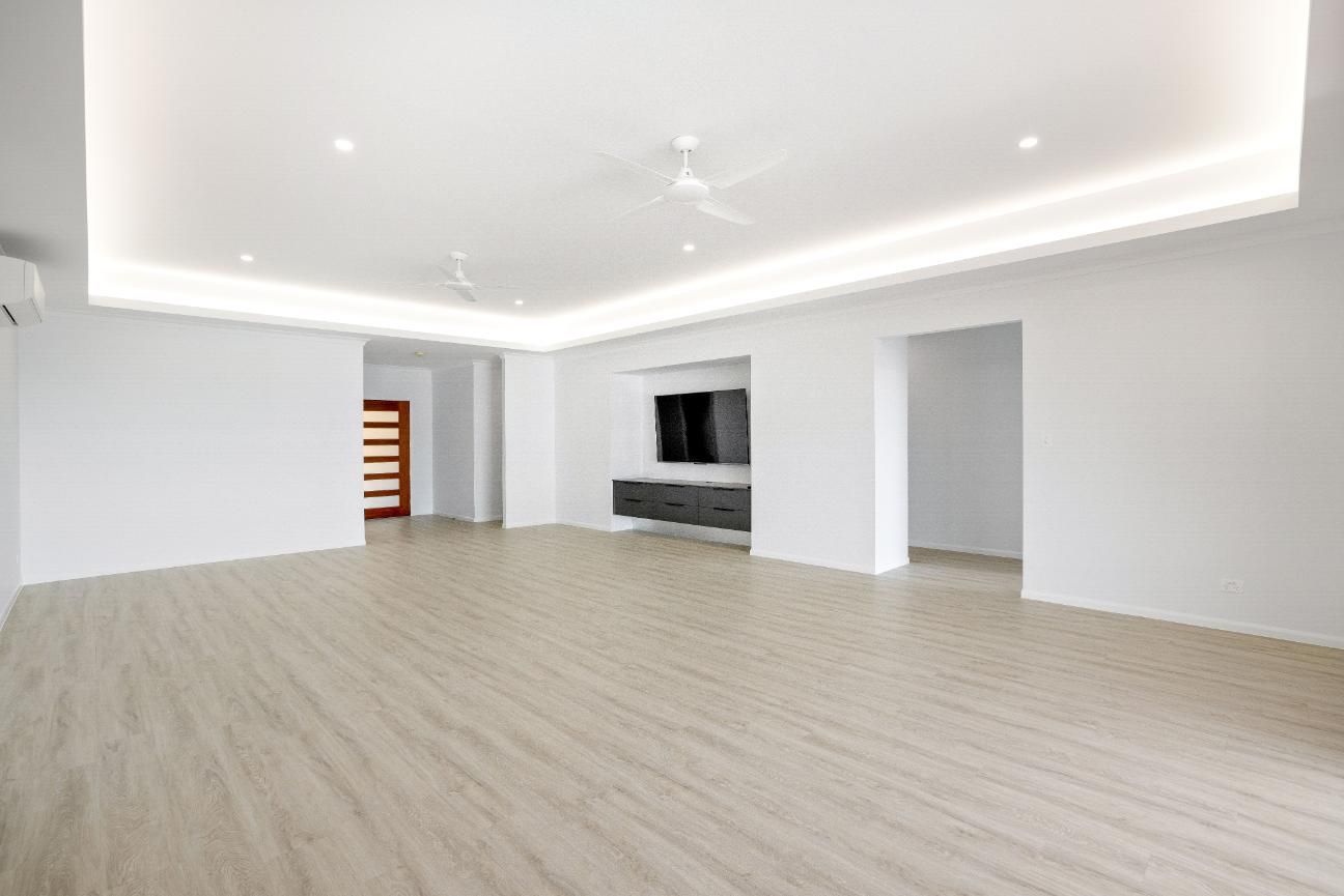 A Large Empty Room With a Wooden Floor and White Walls — Ashlee Jones Homes in Gordonvale, QLD